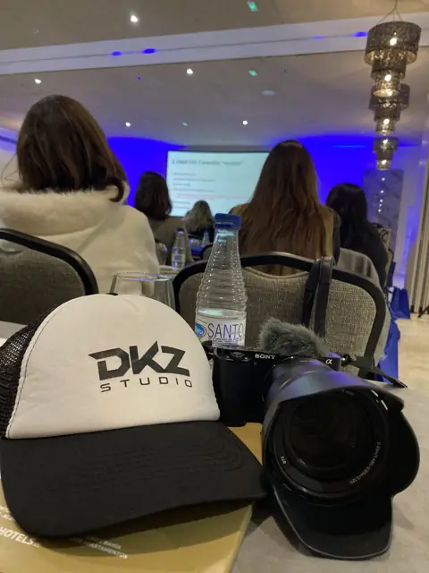 Cámara con objetivo y gorra de DKZ Studio sobre una mesa en un congreso · agencia de marketing y vídeo para negocios de La Alberca