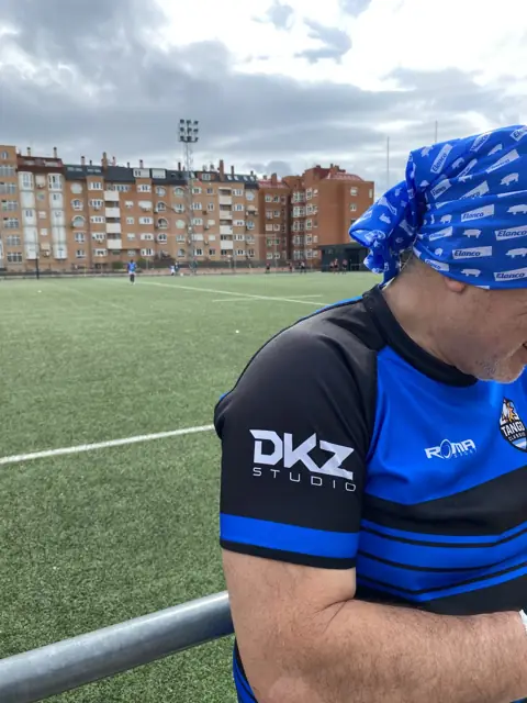 Persona con camiseta deportiva con el logo de DKZ Studio junto a un campo de fútbol · marketing y producción audiovisual para Alcantarilla