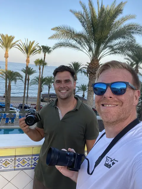 Dos profesionales posan con cámaras ante el mar y las palmeras de un paseo marítimo · marketing y producción audiovisual para Águilas