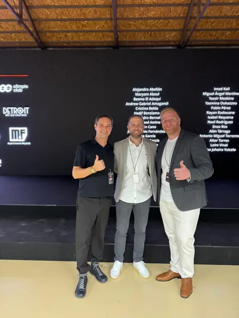 Tres profesionales posan ante un panel oscuro con nombres de ponentes en un evento · agencia de marketing en Murcia y alrededores