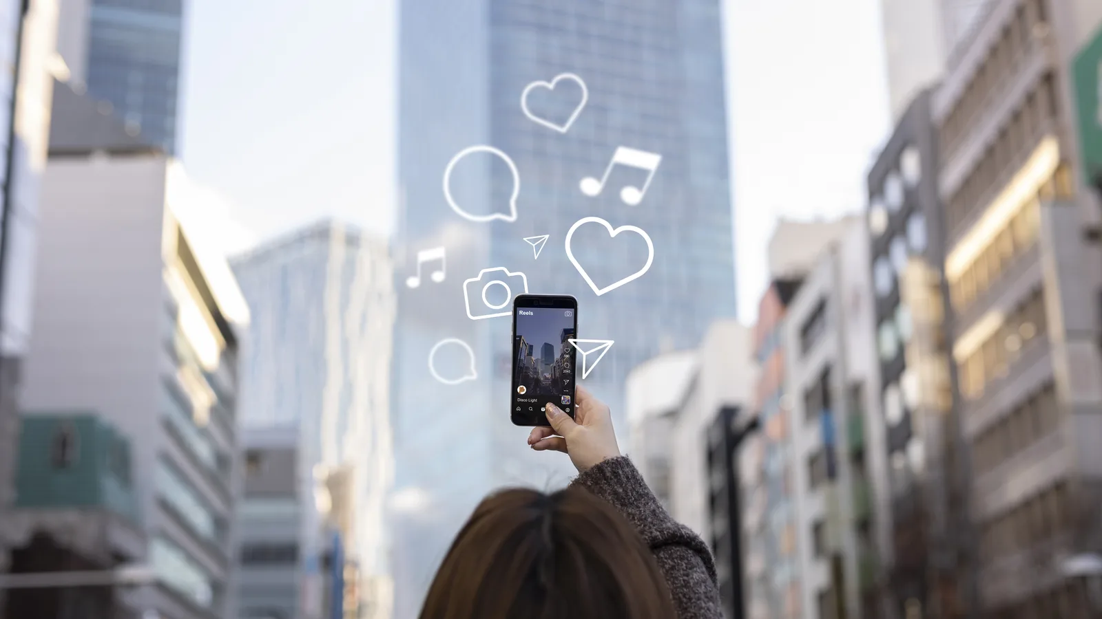 Persona sosteniendo un móvil con un Reel e iconos de redes sociales