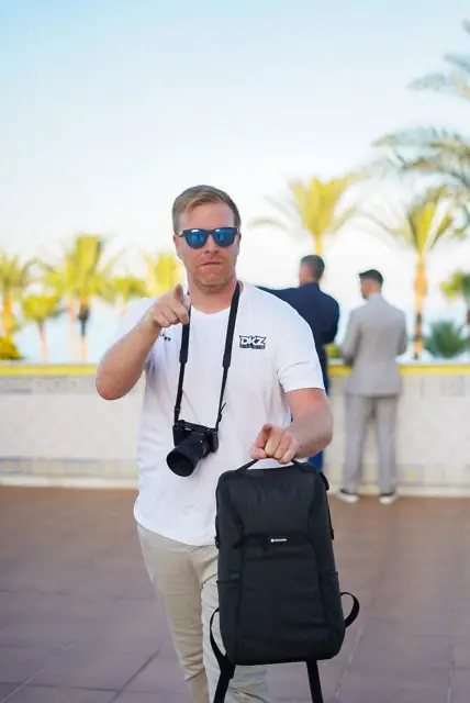 DKZ Studio team member with a camera and backpack on a palm-lined seafront promenade · marketing and video agency for businesses in La Manga